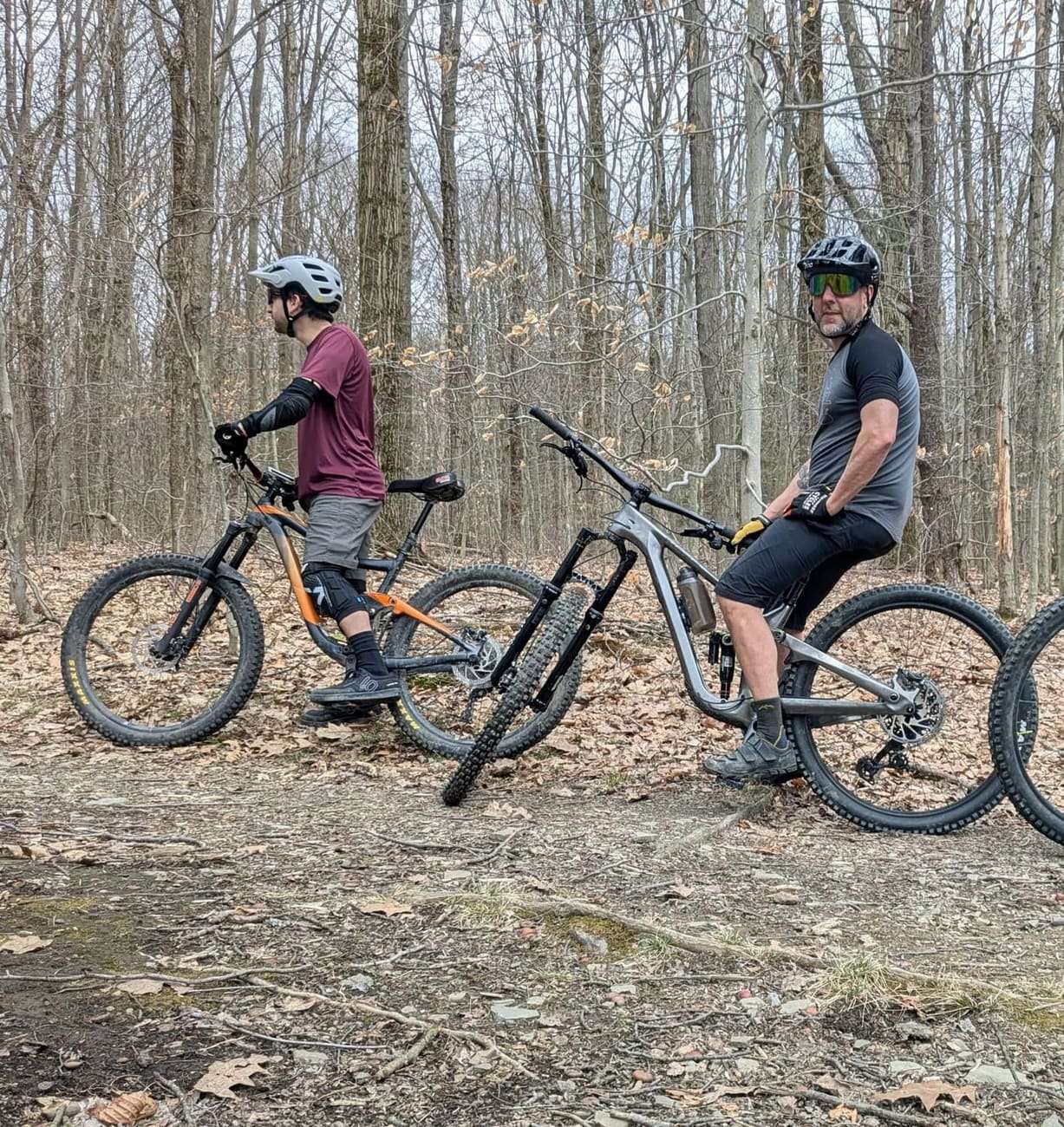 Two riders stopped on a leaf covered trail in the woods