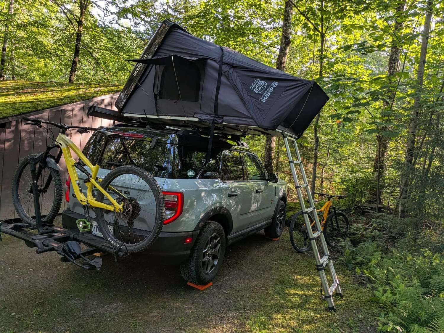 A roof tent open above a truck at a wooded campsite