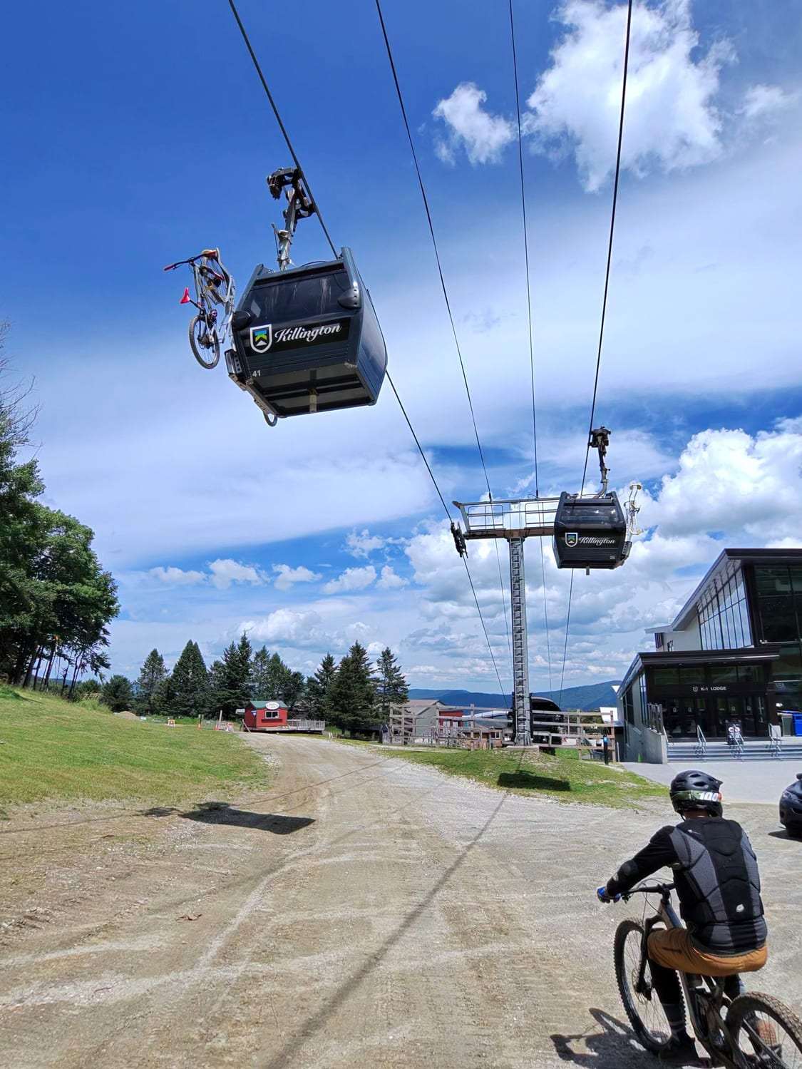 Two gondola cabins carrying mountain bikes up over a ski area on a blue summer day