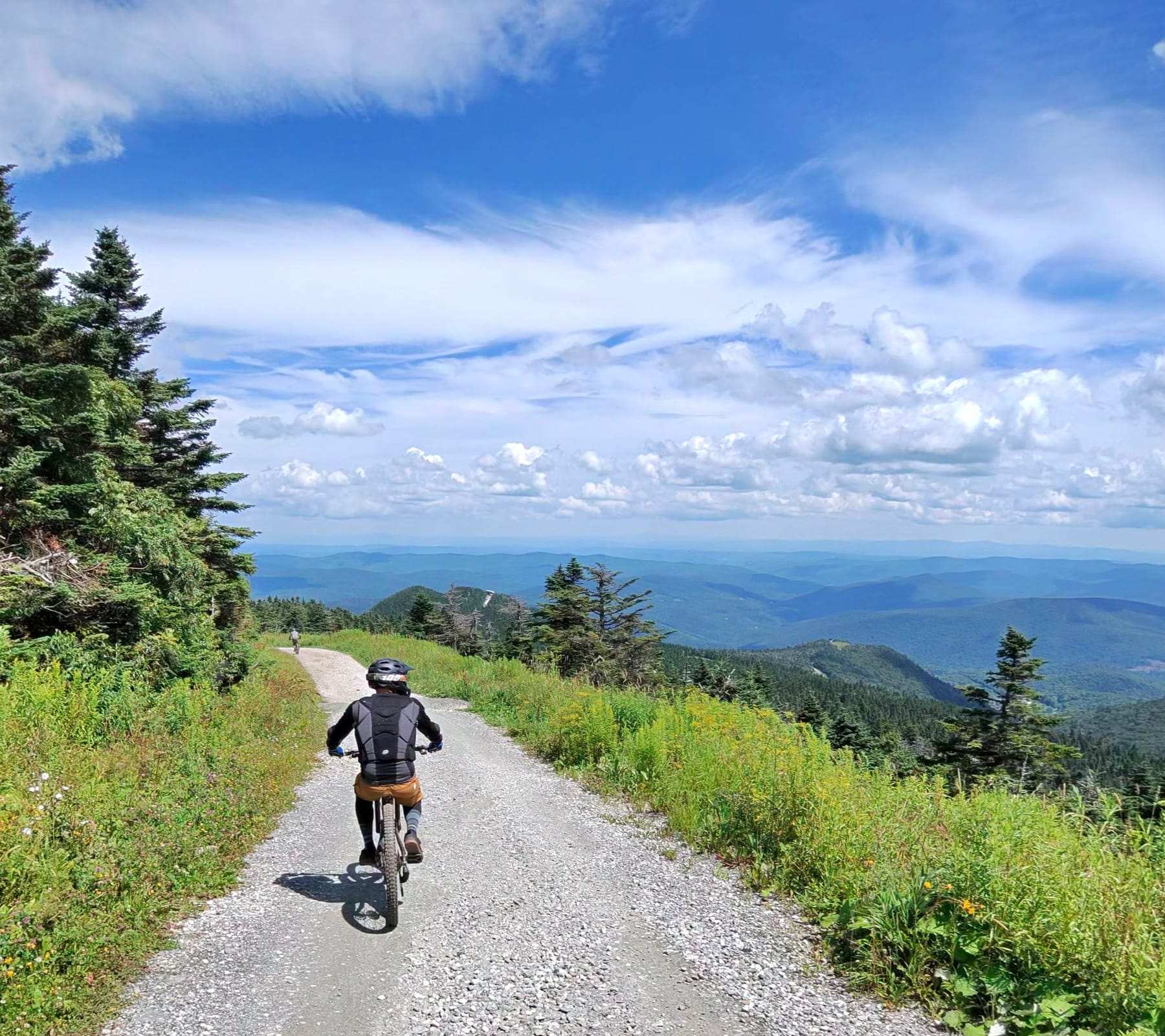 A rider climbing a gravel road along a ridge with mountains and open sky behind