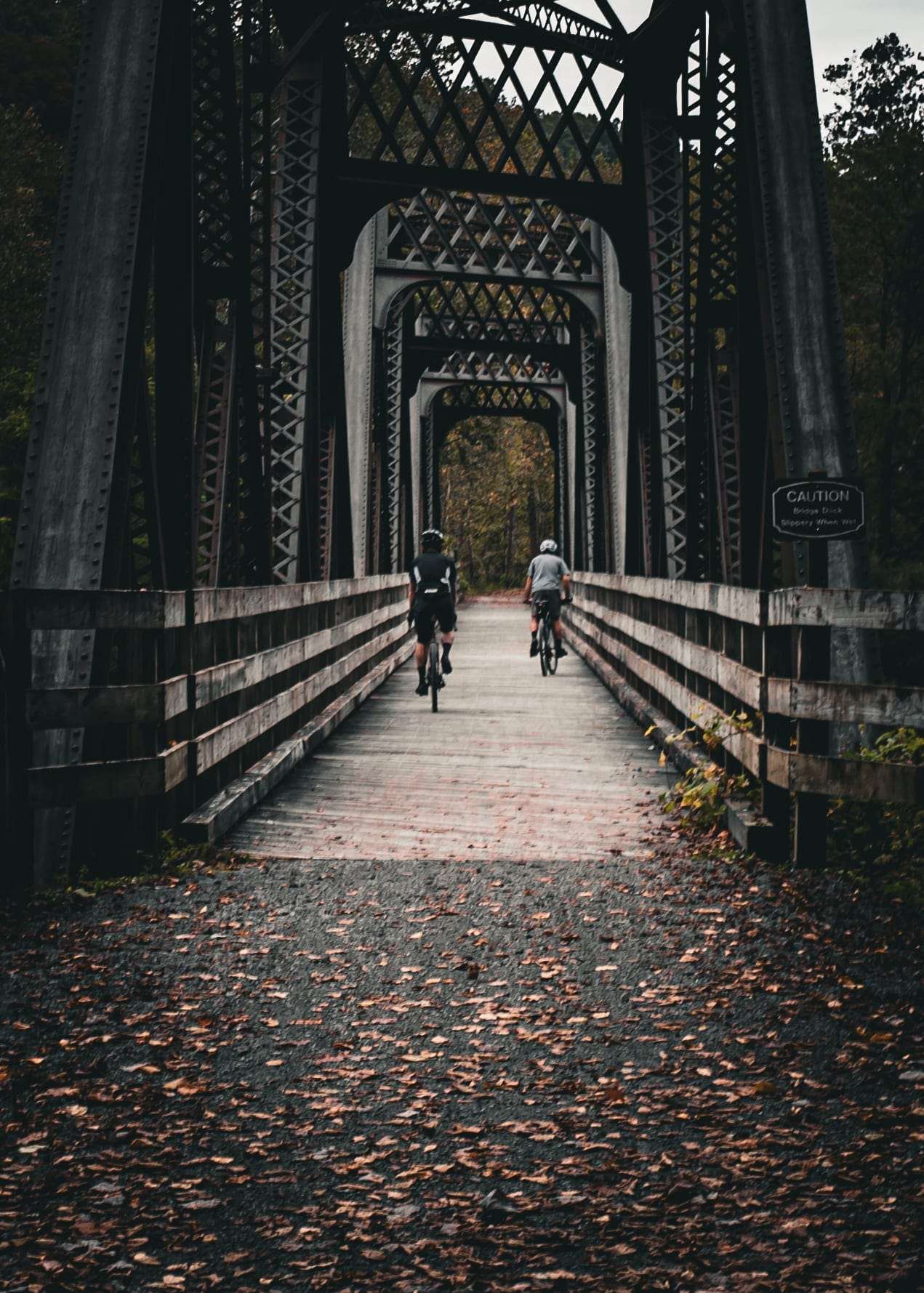 Two riders crossing a steel trestle bridge on a rail trail