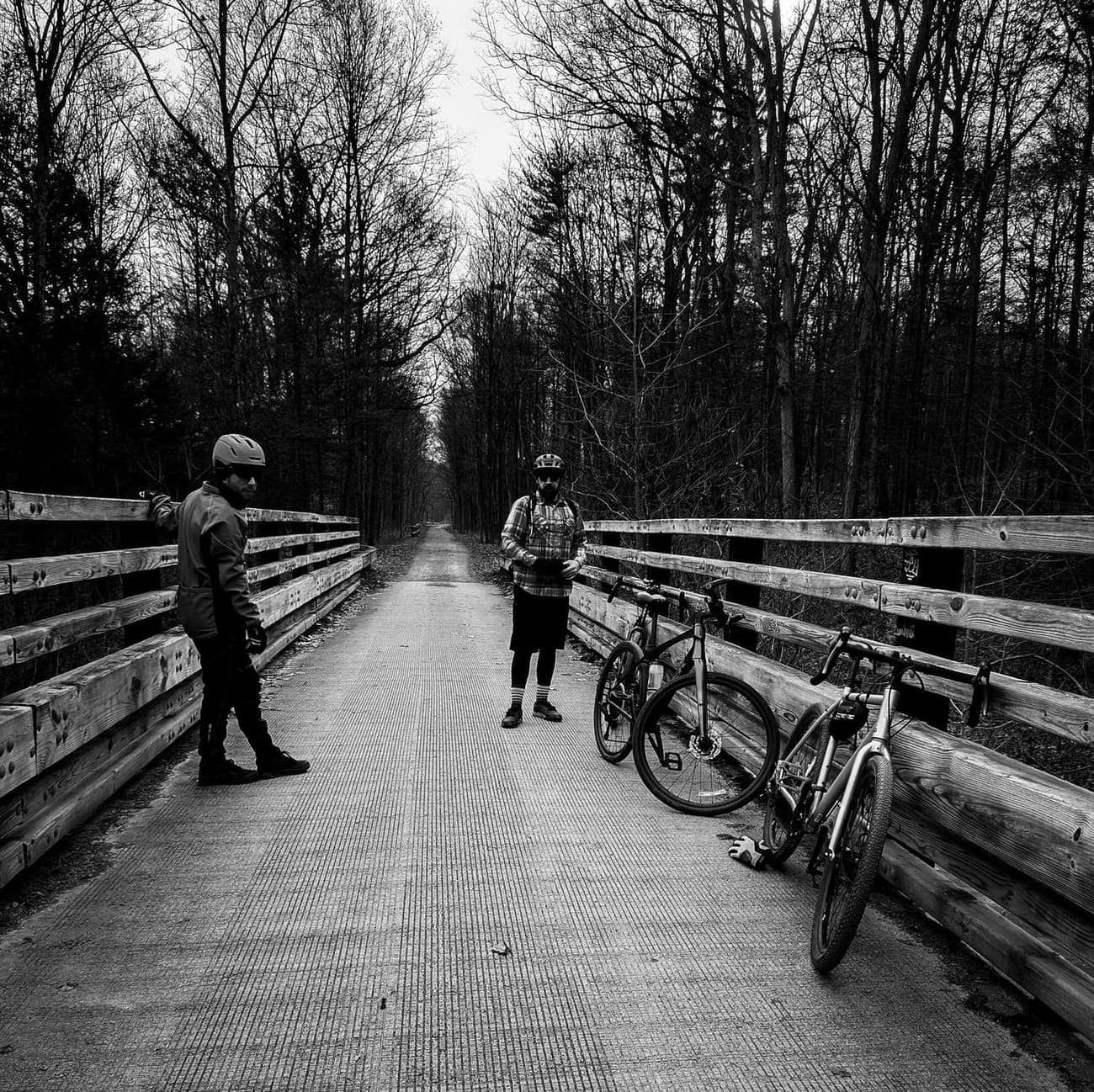 Two riders and their bikes on a winter rail trail, in black and white