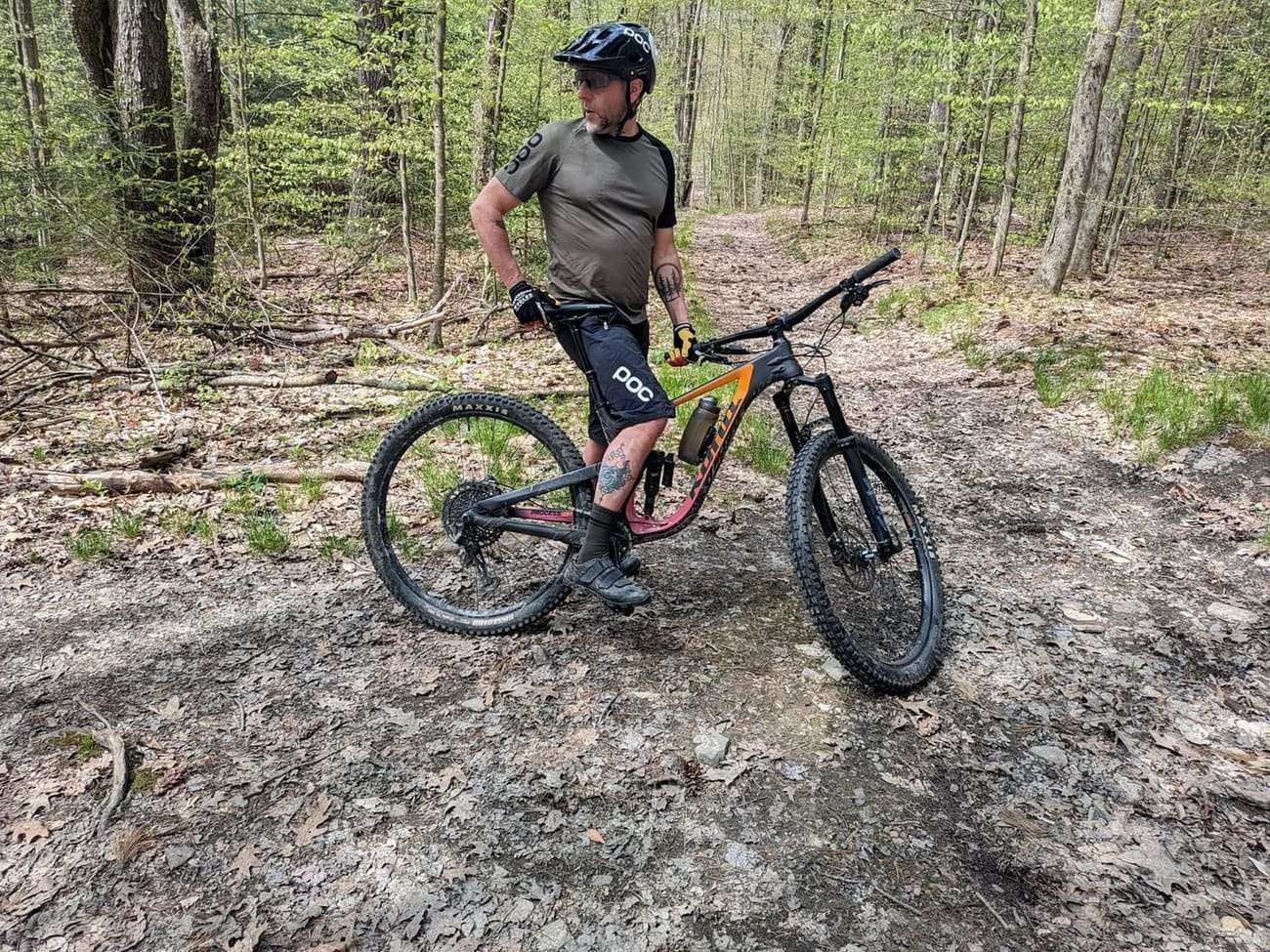 A rider standing with a full suspension bike on a rocky trail